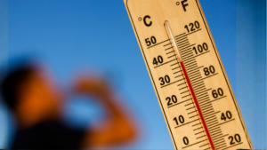 thermostat during heat wave showing temperature 100 derees as man drinks in background