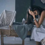 Woman with postpartum depression sitting with her head in her hand by baby bassinet crib